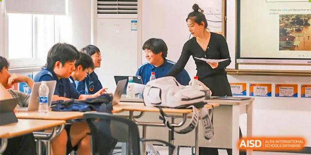 A teacher from Ningbo Huamao International School helping a student at their desk.