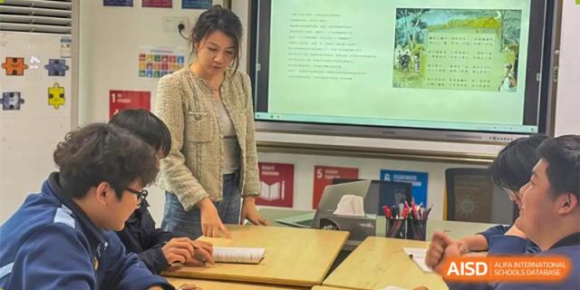 A teacher from Ningbo Huamao International School standing at the front of a classroom, using a laptop and interactive screen.
