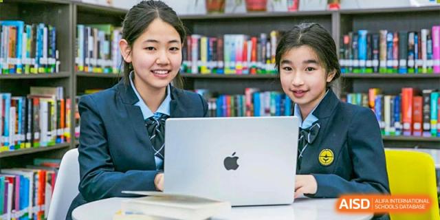 Two students from Ningbo Huamao International School smiling and looking at a laptop in the library.