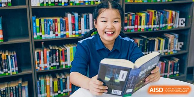 A student from Ningbo Huamao International School smiling while reading a book in the library.
