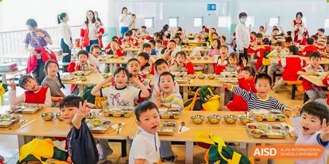 A large group of young students from Ningbo Huamao International School smiling and eating together at a long table.