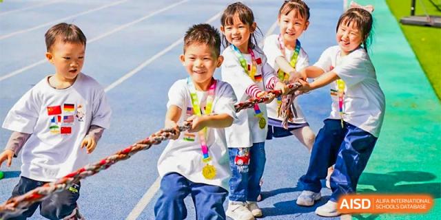 Ningbo Huamao International School students smiling and holding a rope during a fun outdoor activity.