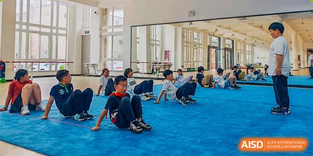 Young students from Ningbo Huamao International School participating in a physical activity on a blue mat.