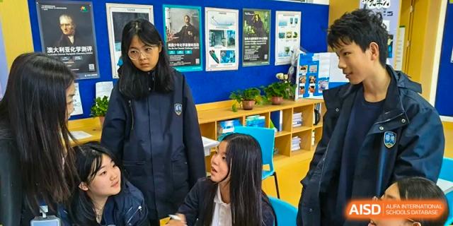 Qingdao MINGDE School student and a teacher talking in a classroom with educational posters on the wall.
