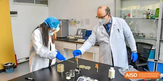 Qingdao MINGDE School teacher and students in lab coats working on a science experiment with petri dishes.