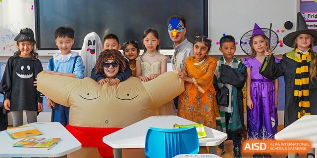 Qingdao MINGDE School students and a mascot posing for a picture in a classroom.