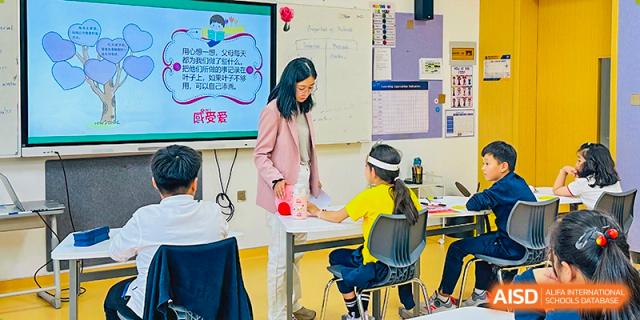 A teacher from Qingdao MINGDE School interacting with a student in a classroom.