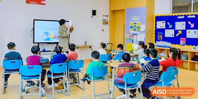 Young Qingdao MINGDE School students sitting at colorful desks in a classroom.