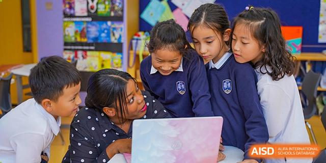 A group of young Qingdao MINGDE School students collaborating on a laptop in a classroom.