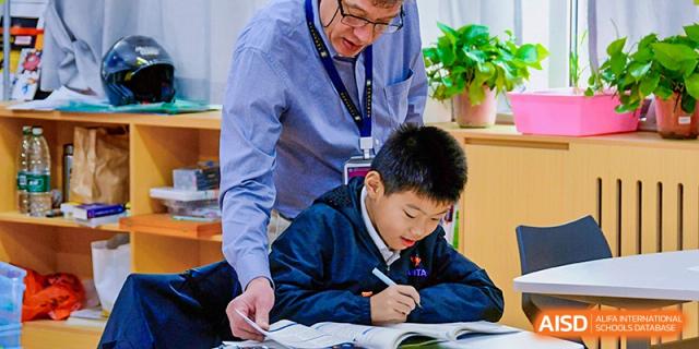 A Qingdao MINGDE School teacher helping a student with his schoolwork.