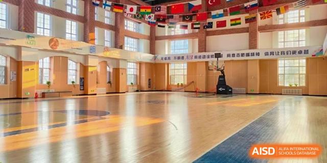 The empty indoor gymnasium at Qingdao MINGDE School with flags from various countries hanging from the ceiling.