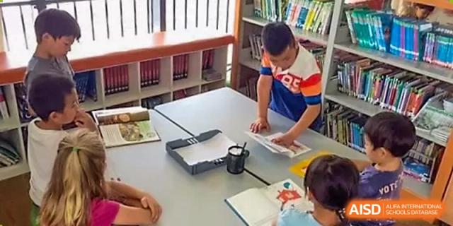 A group of students works together on a laptop at a table in a classroom at Qingdao No.1 International School of Shandong Province (QISS).