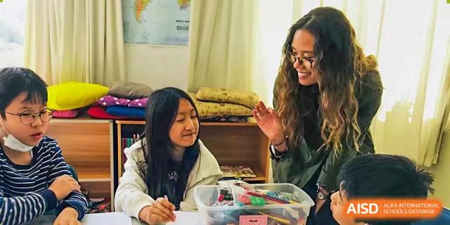 A female student smiles and works with a teacher at her desk in a classroom at Qingdao No.1 International School of Shandong Province (QISS).