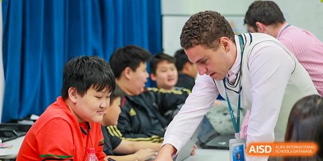 A teacher helps a group of male students with their work in a classroom at Qingdao No.1 International School of Shandong Province (QISS).