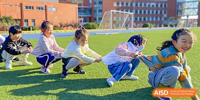Two students play tug-of-war on a green field at Qingdao No.1 International School of Shandong Province (QISS).