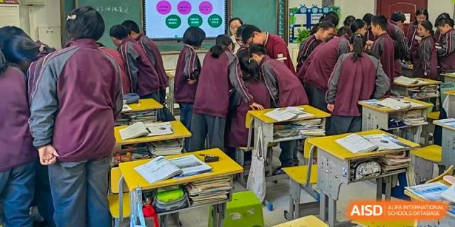 A classroom scene with students in maroon uniforms gathered around a desk and interacting with each other during a lesson at Yichang Tianwen International School.
