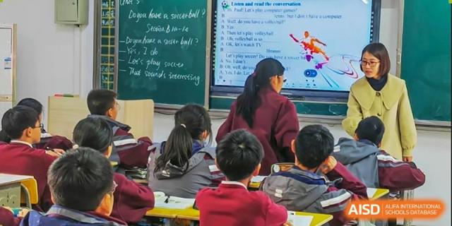 Students attentively sitting in a classroom with a chalkboard visible, showing both written lessons and a screen display at Yichang Tianwen International School.