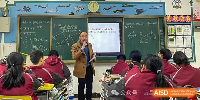 A male teacher speaking into a microphone while standing in front of the class, with a presentation screen visible on the chalkboard at Yichang Tianwen International School.
