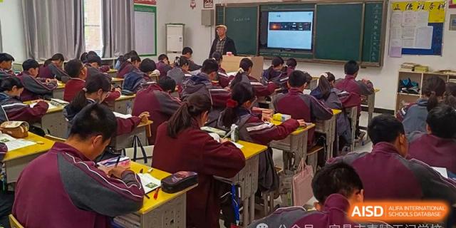 A classroom full of students in maroon uniforms diligently taking notes at their desks during a lesson at Yichang Tianwen International School.