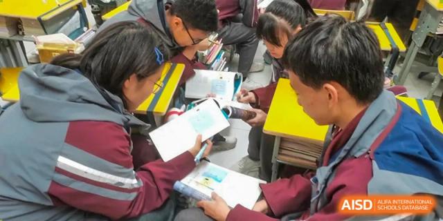 A group of students in uniform gathered closely together, sharing and reviewing materials from textbooks during a group activity at Yichang Tianwen International School.