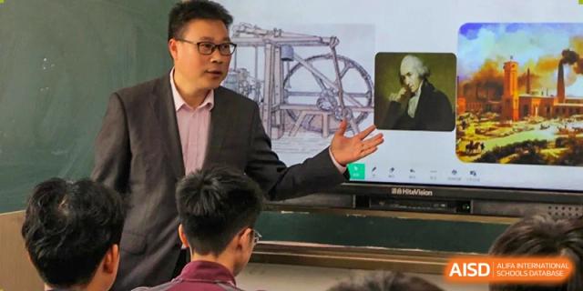 A teacher pointing to a complex mechanical diagram displayed on a screen while instructing students in a science or engineering class at Yichang Tianwen International School.