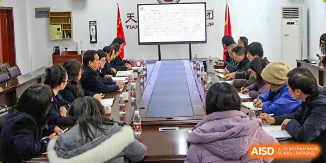 Students and staff seated around a large conference table in a meeting room, looking at a presentation displayed on a white screen at Yichang Tianwen International School.