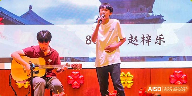 A male student singing into a microphone on stage during a performance or event at Yichang Tianwen International School.