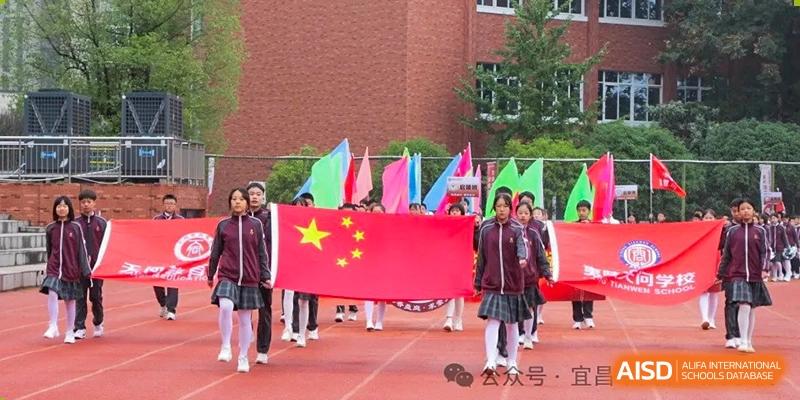 A group of students carrying the national flag of China and other colorful flags while marching on a red running track at Yichang Tianwen International School.