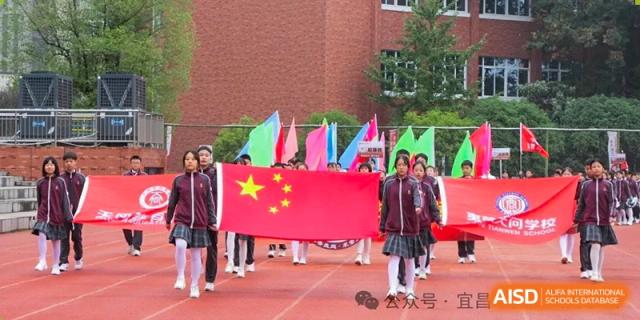 A group of students carrying the national flag of China and other colorful flags while marching on a red running track at Yichang Tianwen International School.