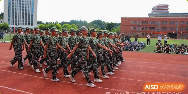 A large group of students in military-style camouflage uniforms standing in formation on a red track during a drill at Yichang Tianwen International School.