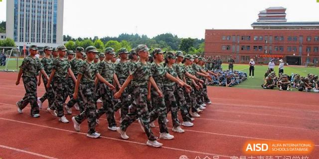 A large group of students in military-style camouflage uniforms standing in formation on a red track during a drill at Yichang Tianwen International School.