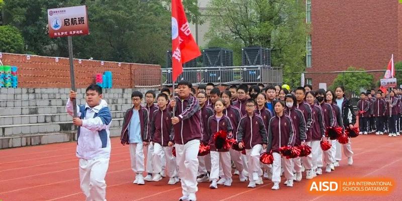 A line of students in maroon and white uniforms marching with red flags and pompoms during an outdoor school parade or event at Yichang Tianwen International School.