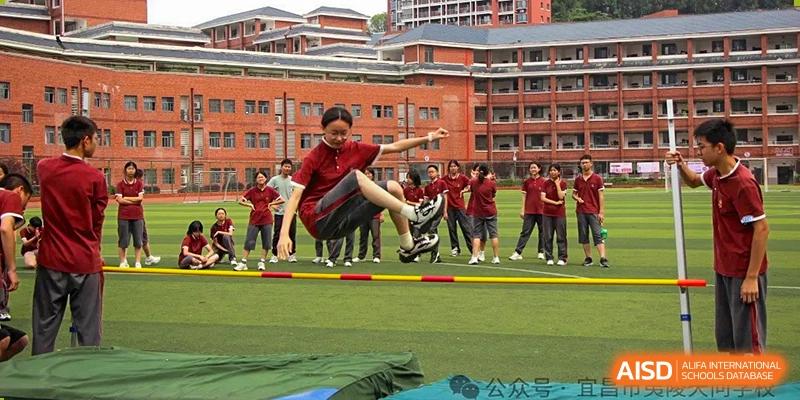 A student performing a jumping event, leaping over an obstacle outdoors in front of other cheering students at Yichang Tianwen International School.