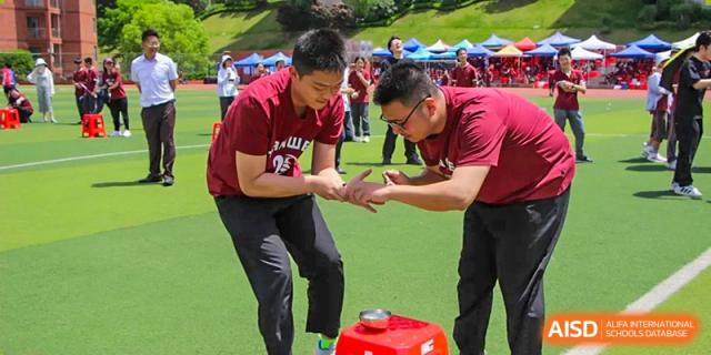 Two students in maroon uniforms participating in an outdoor game or team-building activity during a school fair at Yichang Tianwen International School.