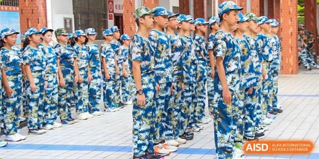 A line of students wearing blue camouflage uniforms and caps standing in a disciplined formation outdoors at Yichang Tianwen International School.
