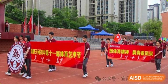 A student in a red uniform standing on a sports field during an art or sports event, with tents and banners in the background at Yichang Tianwen International School.