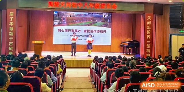 Two students on a stage performing in front of a large audience seated in rows in an auditorium at Yichang Tianwen International School.