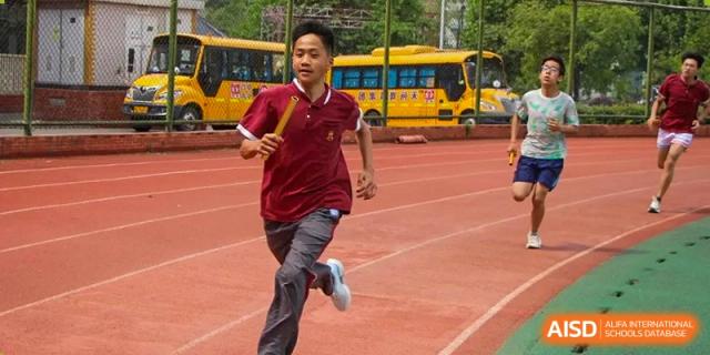 A male student in a maroon polo shirt running with a relay baton on the red track at Yichang Tianwen International School.