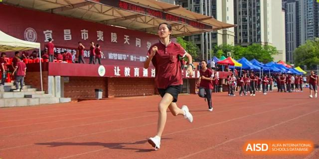 A female student in a maroon shirt and shorts running on the red track during a sports activity or race at Yichang Tianwen International School.