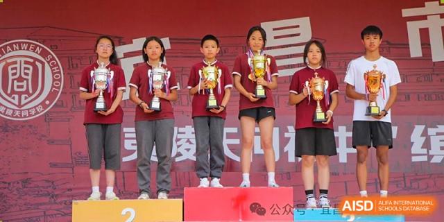 Students standing on a podium holding red and gold trophies after winning a competition or sports event at Yichang Tianwen International School.