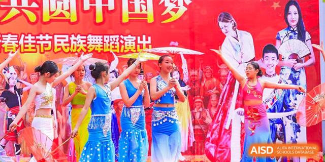 Students from Shenzhen Oasis International School performing a dance on stage in blue costumes.