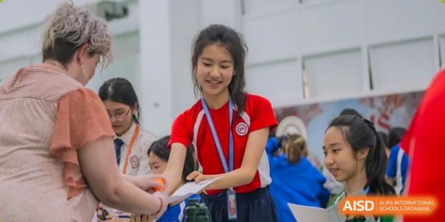 A female student from Shenzhen Oasis International School hands out a flyer at a school event.