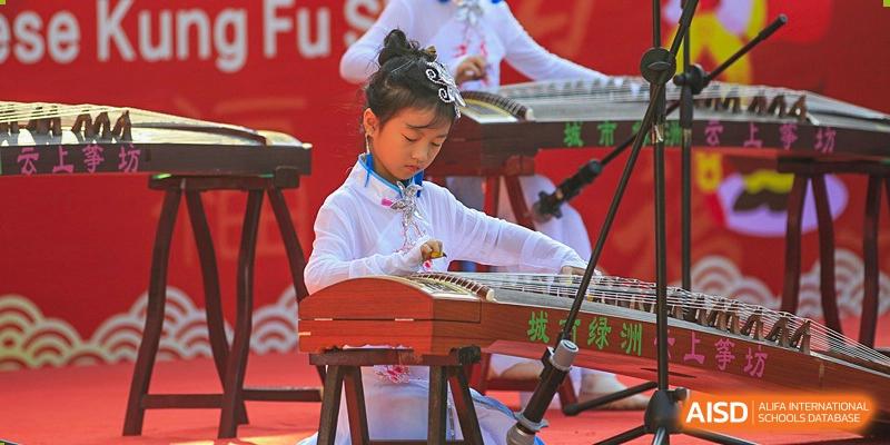 A young female student from Shenzhen Oasis International School plays a traditional Chinese string instrument.
