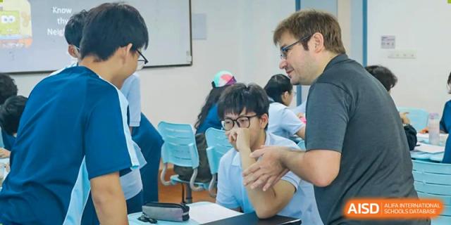 A teacher from World Leading Schools Association interacting closely with a student at his desk during a lesson.