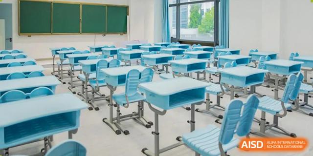 An empty modern classroom at World Leading Schools Association with rows of blue desks and chairs.