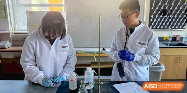 Students from World Leading Schools Association wearing lab coats and conducting an experiment involving glassware in a science lab.