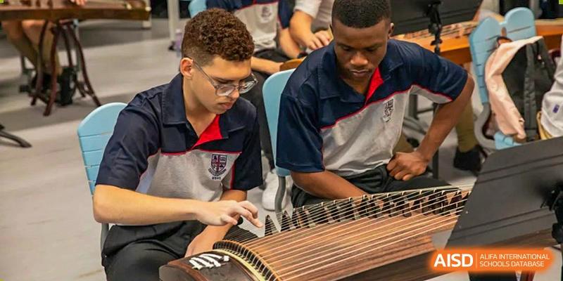 Two students from World Leading Schools Association in uniform practicing a musical instrument (a Guzheng or similar zither).