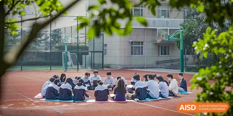 A group of students from World Leading Schools Association sitting in a circle outdoors on the campus lawn, talking.