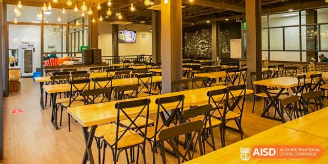 The empty, warmly lit dining hall or cafeteria at World Leading Schools Association with rows of wooden tables and chairs.