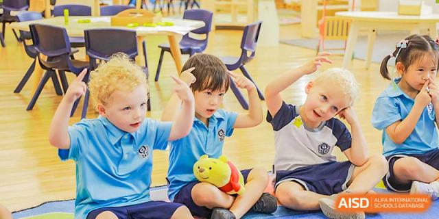 Harrow International School Shenzhen young students in uniform participating in a classroom activity, one holding a yellow toy.